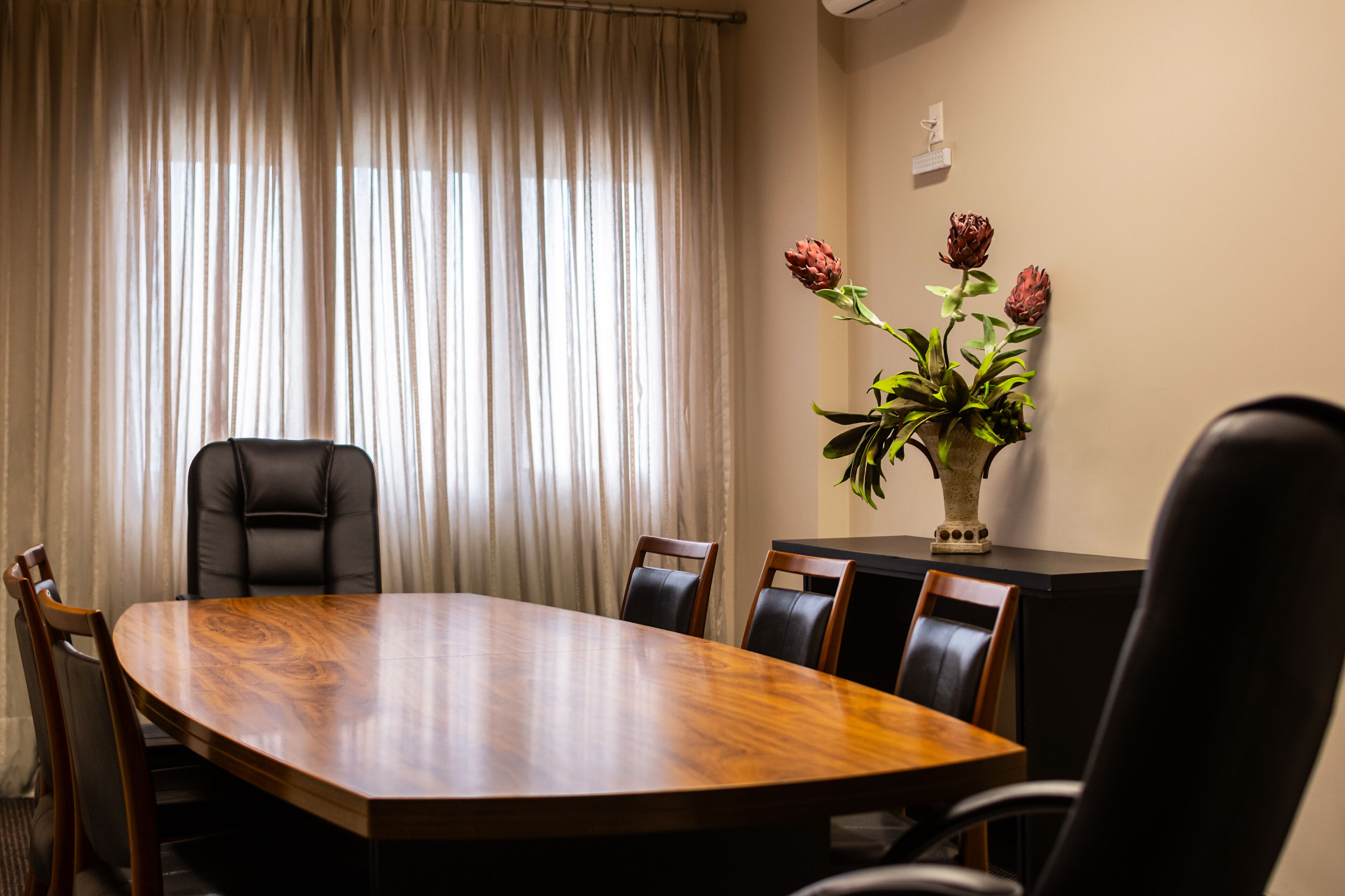 Een vergaderruimte met een houten tafel, zwarte lederen stoelen en een vaas met bloemen op een tafel.