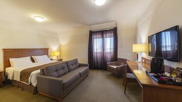 A hotel room with a bed, a sofa, a desk, a chair, a television, and a window with curtains.