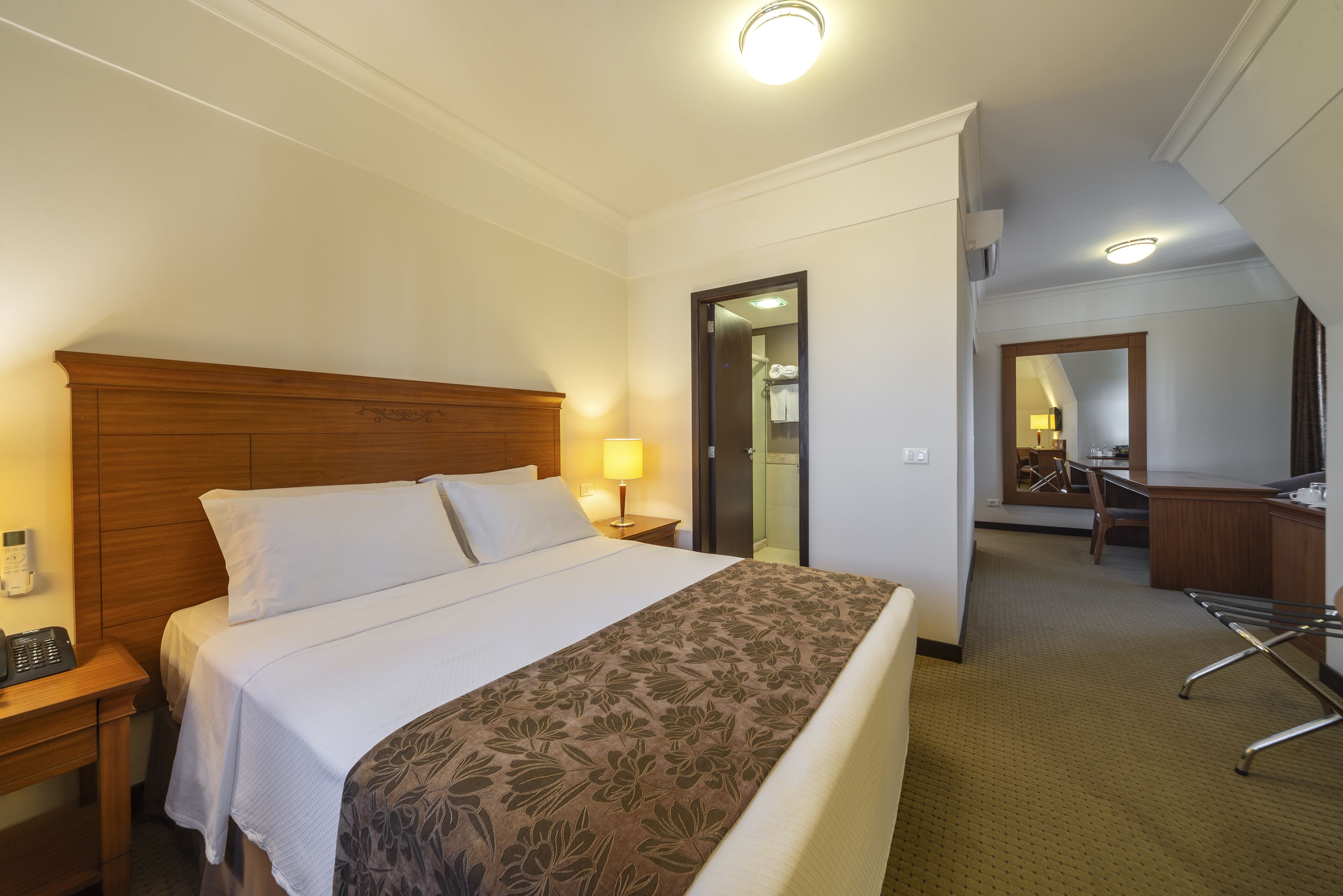 Habitación de hotel con cama, mesita de noche, lámpara y escritorio con silla.