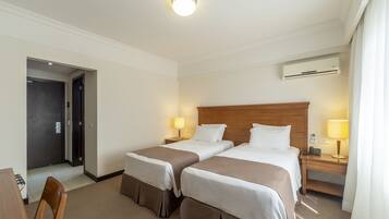 A hotel room with two beds, a desk, a chair, a door, and an air conditioning unit.