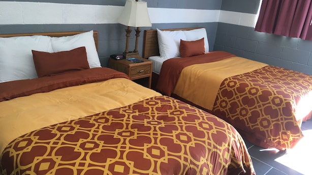 Habitació d'hotel amb dos llits, cadascun amb roba de llit estampada, una cambrera de nit amb una làmpada i una paret amb un disseny a ratlles.