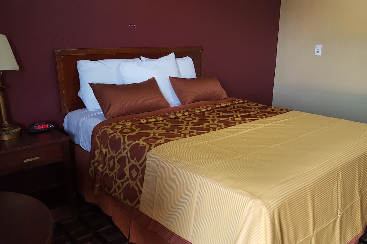 A hotel room with a bed, a nightstand, a lamp, and a digital clock displaying the time.