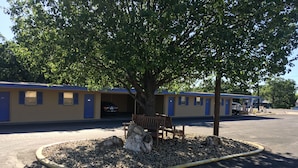 Motel amb una zona d'aparcament, un arbre i una banca.
