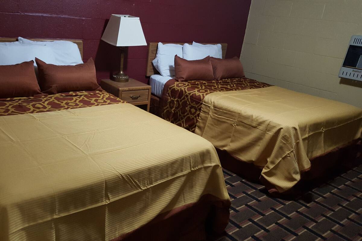 Two single beds with patterned bedspreads, a nightstand with a lamp, and a wall-mounted air conditioning unit.