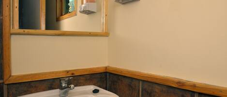 A bathroom with a white sink, wooden paneling, and a mirror.