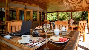 An outdoor wooden dining area with a laptop, wine glasses, and a plate of watermelon.