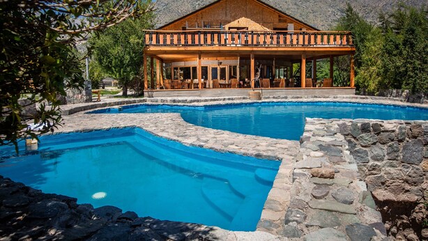 A resort with a pool, wooden deck, and mountain backdrop.