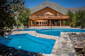 A resort with a pool, wooden deck, and mountain backdrop.