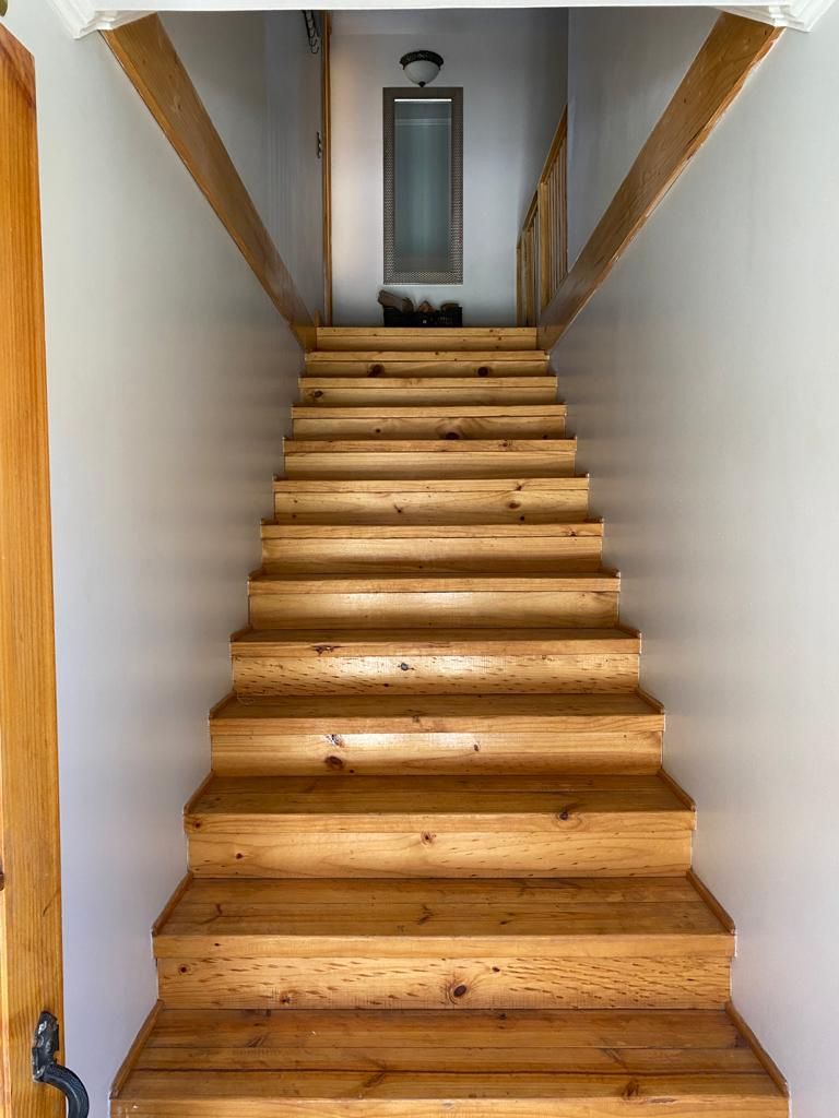 Een houten trap met een leuning aan de linkerkant, leidend naar een plateau met een deur en een lamp.