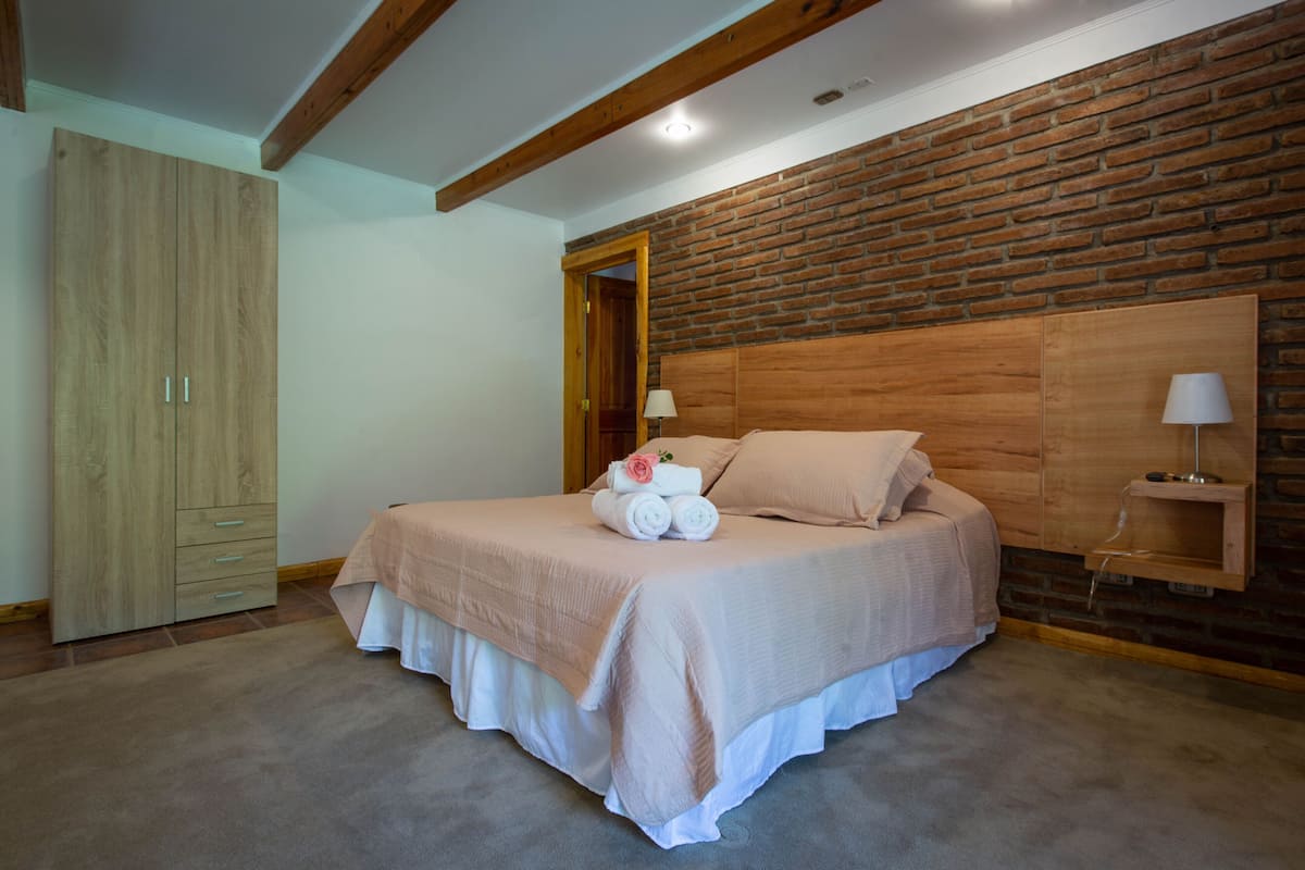 Un dormitorio con cabecera de madera, un armario, una cama con colcha rosa y dos lámparas de noche.
