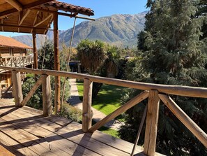 Una terraza de madera con barandilla, un camino y montañas al fondo.