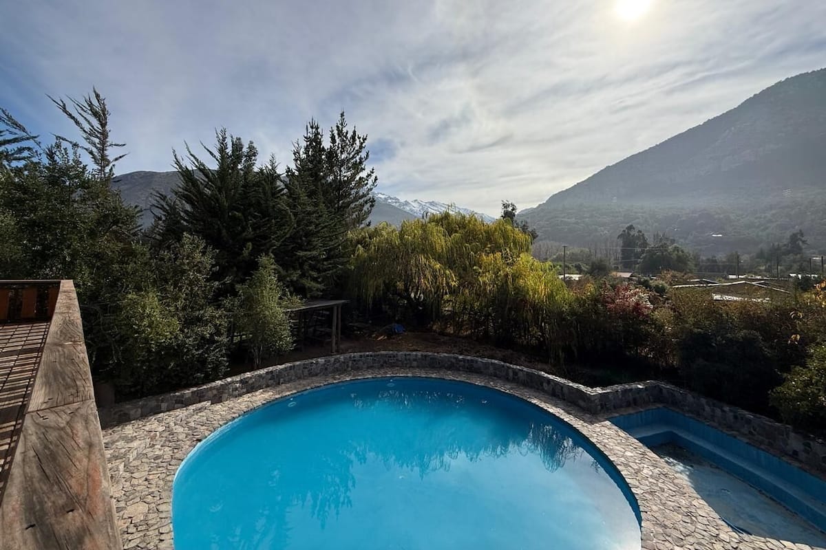 Una piscina rodeada de muros de piedra y abundante vegetación, con una montaña al fondo.