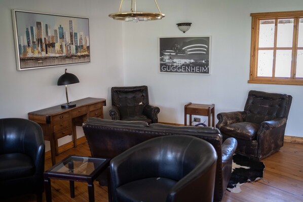 A living room with leather furniture, a cityscape painting, a black and white photo, and a window with wooden frames.