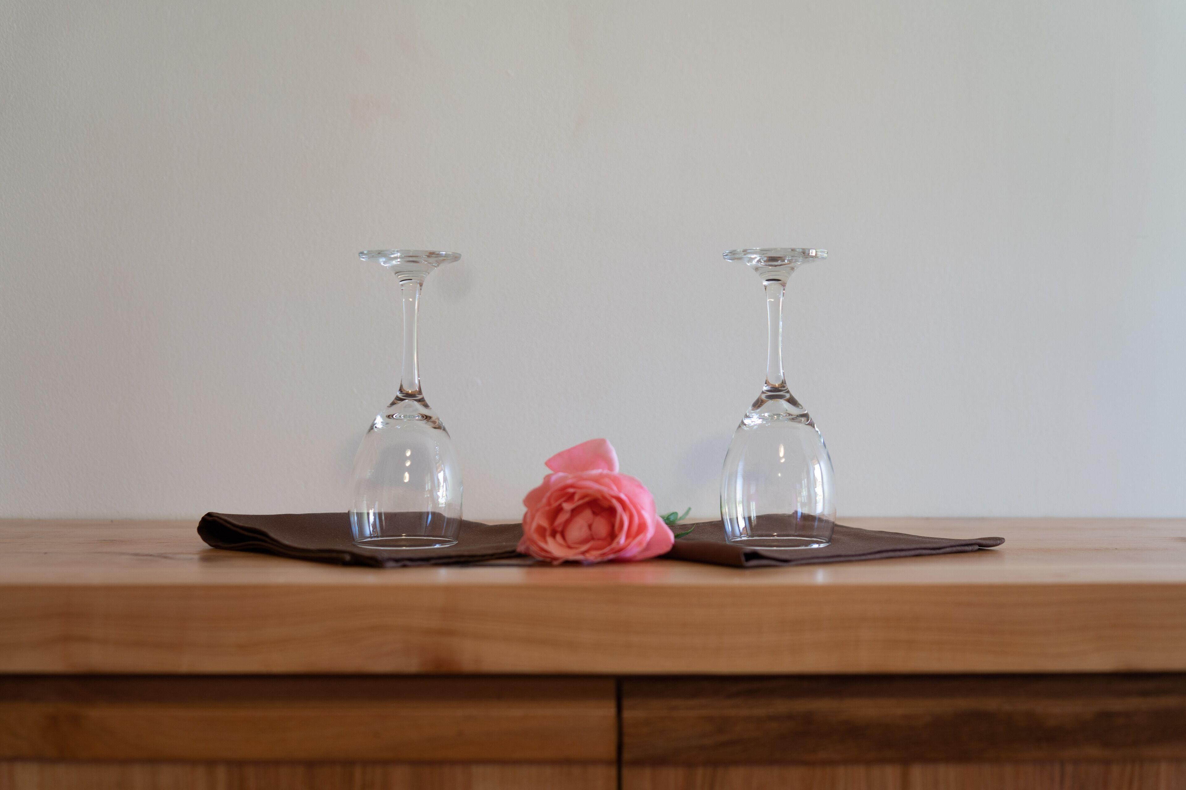 Dues copes de vi sobre una taula de fusta amb una rosa rosa a mig camí.