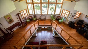 A spacious room with wooden flooring, a central wooden staircase, and large windows offering a view of palm trees.