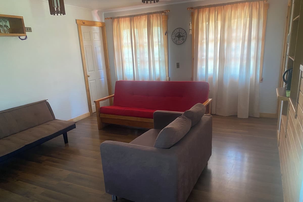 Una sala de estar con un sofá rojo, un sofá gris y suelo de madera.