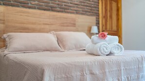 A neatly made bed with a pink pillow, a stack of white towels with a pink rose, and a wooden headboard against a brick wall.