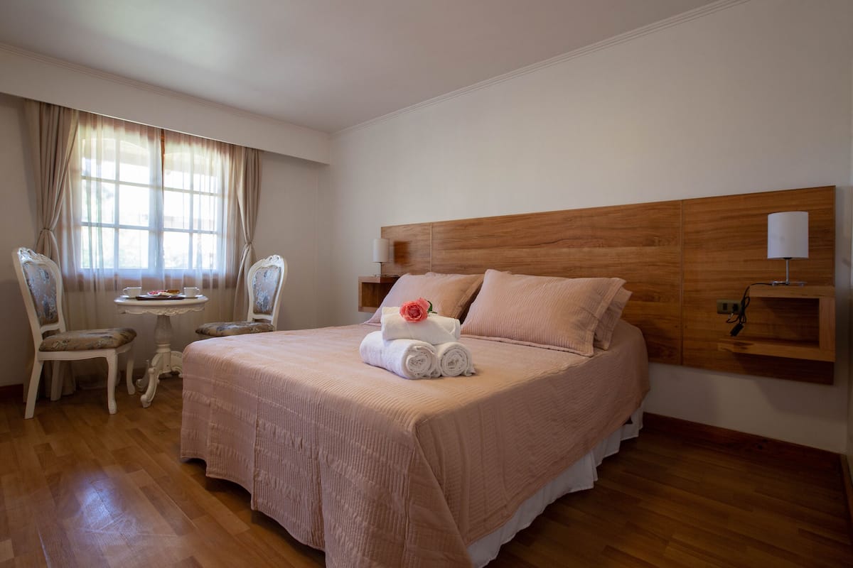 Un dormitorio ordenado con una cama grande, una mesita de noche con una lámpara y una silla.