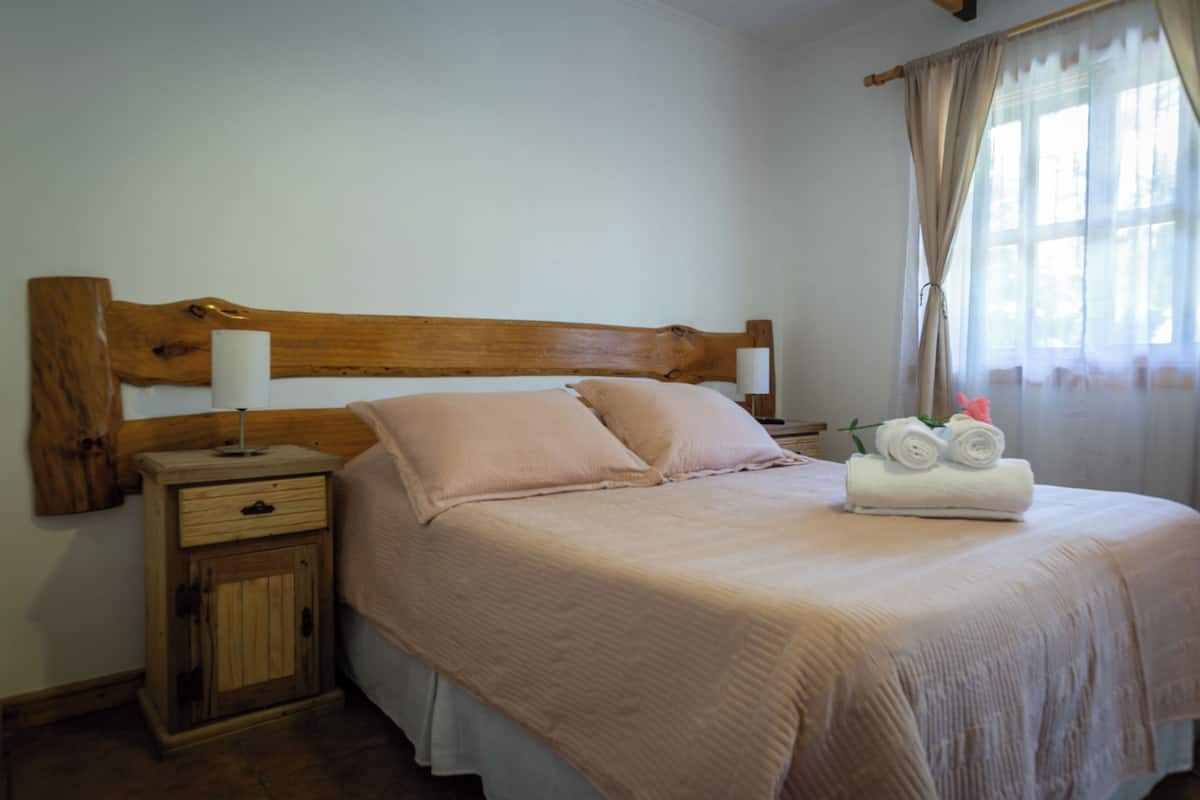 Una cama bien hecha con un cabecero de madera, una mesita de noche con una lámpara y un pequeño armario.