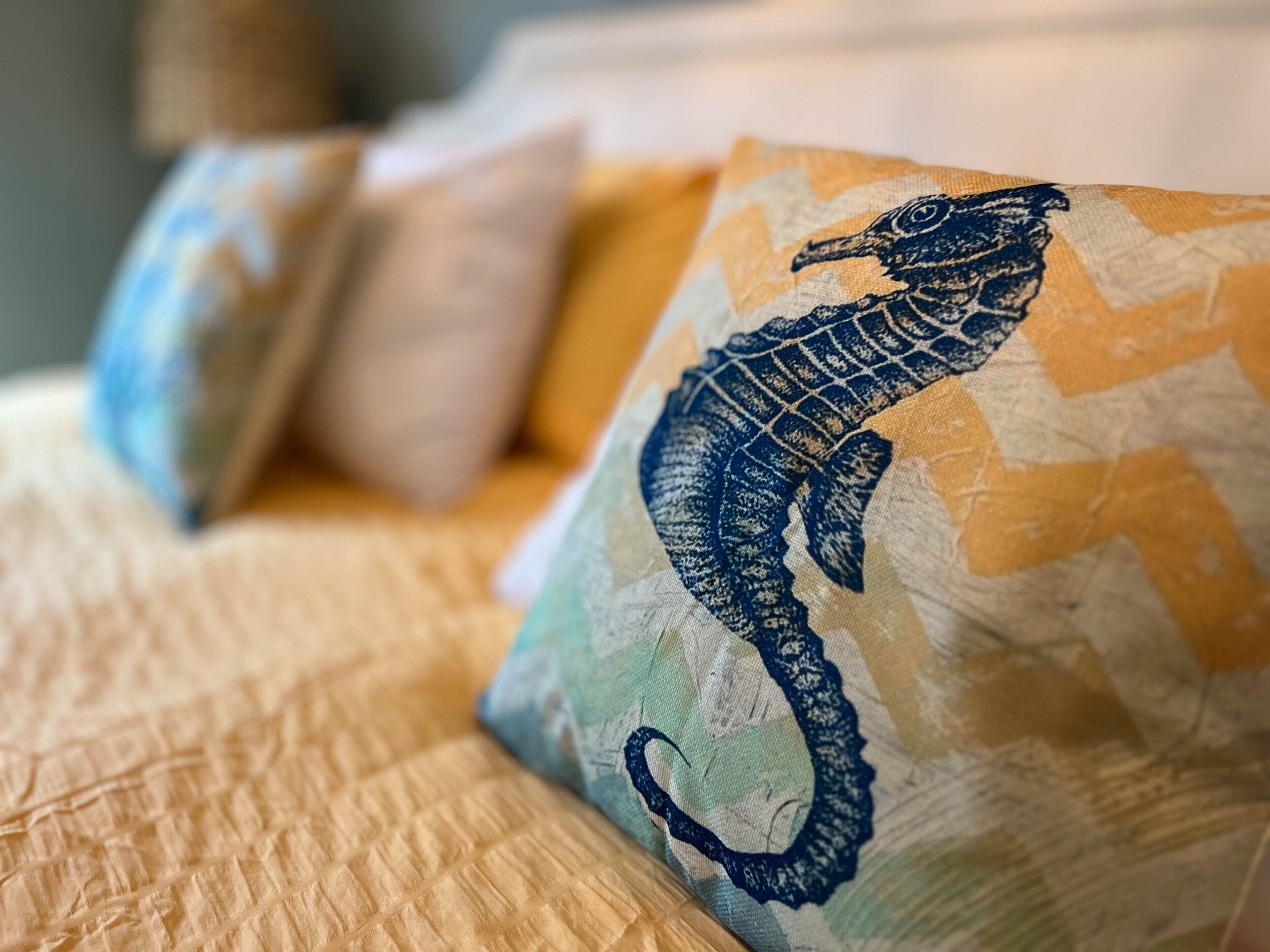 A bed with a textured beige cover and pillows featuring a seahorse design.