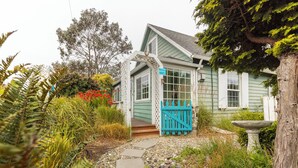 A house with a porch, a blue gate, and a garden with stepping stones. - Enchanted Cottages (Seaview)