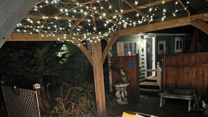 An outdoor seating area with a fire pit, wooden furniture, and string lights. - Enchanted Cottages (Seaview)