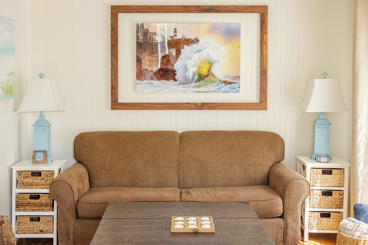 Ein Wohnzimmer mit einem braunen Sofa, zwei Beistelltischen mit Lampen und einem gerahmten Bild an der Wand.