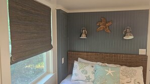 A bedroom with a bed, a window with a blind, and wall-mounted lamps. - Enchanted Cottages (Seaview)