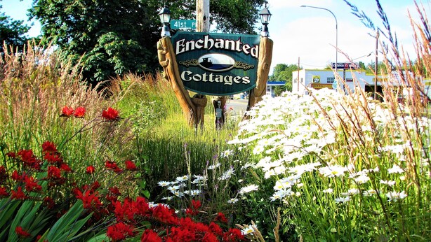 A sign for Enchanted Cottages with a rustic wooden post and a lamp post. - Enchanted Cottages (Seaview)
