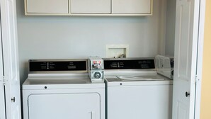 A laundry room with two washing machines, a dryer, and a cabinet above.