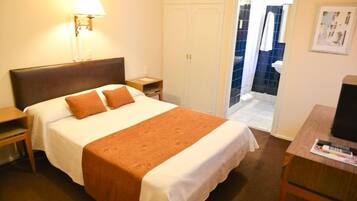 A hotel room with a bed, a nightstand, a lamp, a wardrobe, and a view of the bathroom.