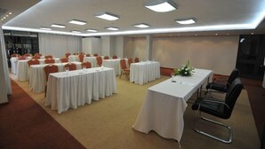 Un salón de conferencias con varias mesas redondas y sillas, equipado con luces de techo y piso alfombrado.
