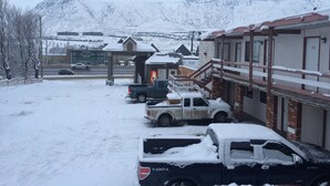 A snow-covered parking area with several vehicles, including a pickup truck and a van, parked in front of a building with a sign that reads "Tyvek." - Rider's Inn (Kamloops)