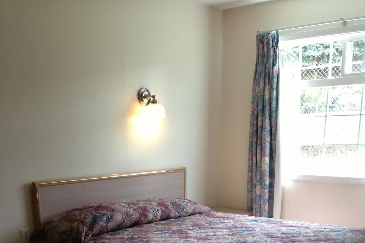 A bedroom with a bed, a nightstand, a lamp, and a window with curtains.