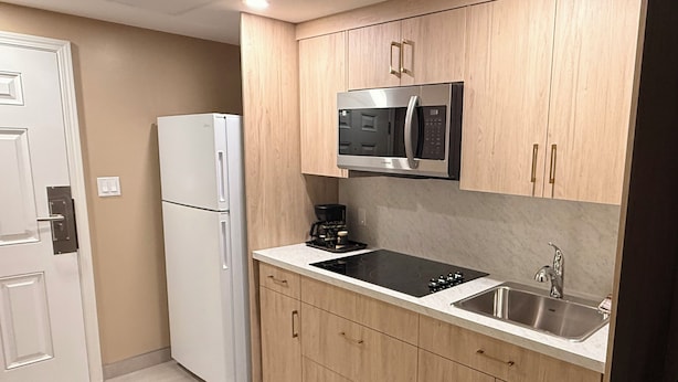 A compact kitchen with a built-in microwave, a stovetop, and a sink. - Rider's Inn (Kamloops)