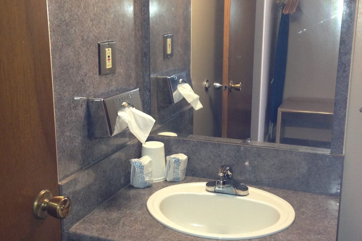 A bathroom with a marble countertop, a white sink, and a mirror. There are two paper towel dispensers and a hand dryer.