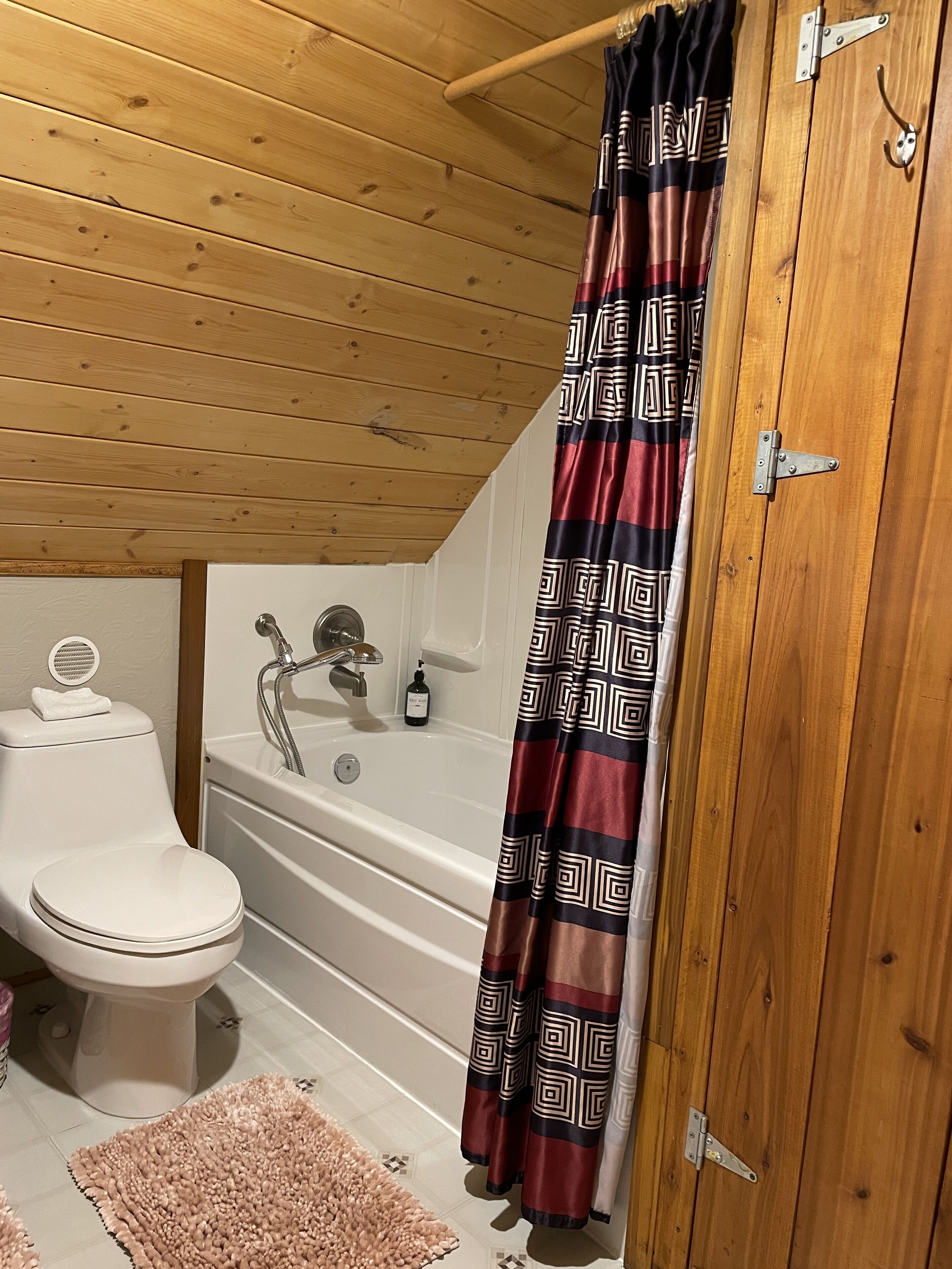 A bathroom with a white toilet, a bathtub, and a shower curtain with a geometric pattern.