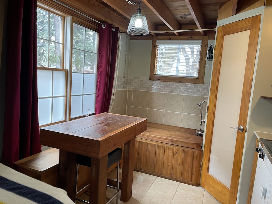 Una cocina compacta con una mesa de madera, una ventana con cortinas, un lavamanos integrado y una puerta.