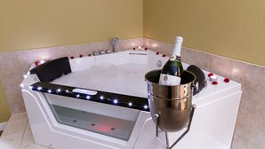 A corner bathtub with rose petals and a champagne bottle. - Park West Inn (Winnipeg)
