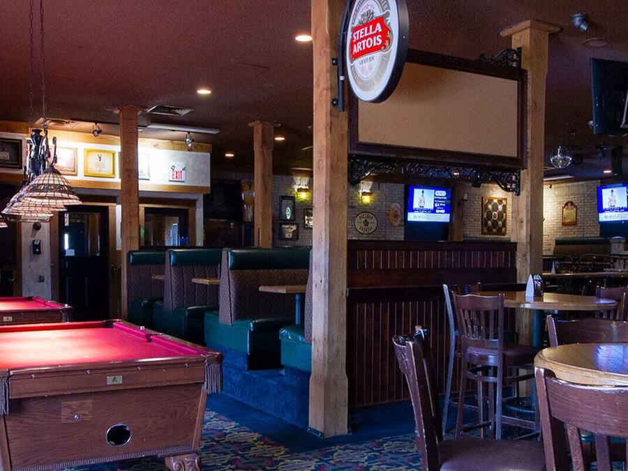 A bar area with pool tables, seating, and a television screen.