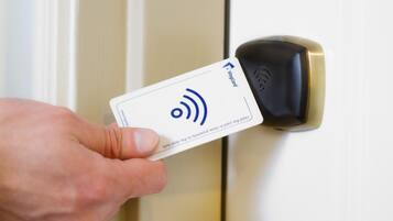 A hand holding a card with a wireless symbol, inserted into a door lock.