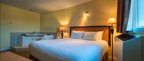 A hotel room with a bed, bedside lamps, a desk, and a small kitchenette.