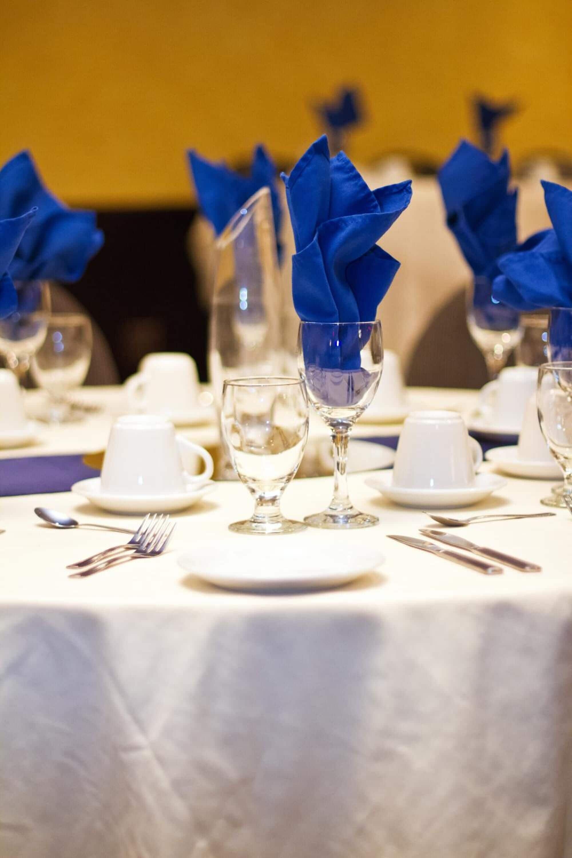 A table set with white cups, clear wine glasses, and blue napkins.