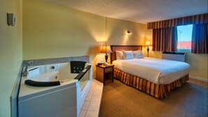 A hotel room with a large bed, a separate bathroom with a bathtub, a bedside table with a lamp, and a window with curtains. - Park West Inn (Winnipeg)