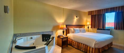 A hotel room with a large bed, a separate bathroom with a bathtub, a bedside table with a lamp, and a window with curtains.
