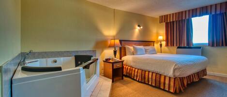 A hotel room with a bed, a nightstand, a lamp, a window with curtains, and a bathtub.
