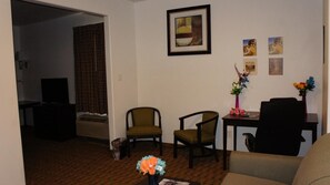 A living room with a sofa, two chairs, a small table with a vase of flowers, and a painting on the wall.