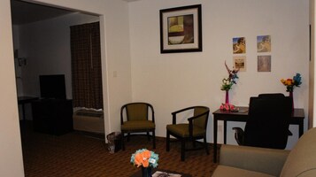 Una sala de estar con un sofá, dos sillones, una mesita con un florero y un cuadro en la pared.