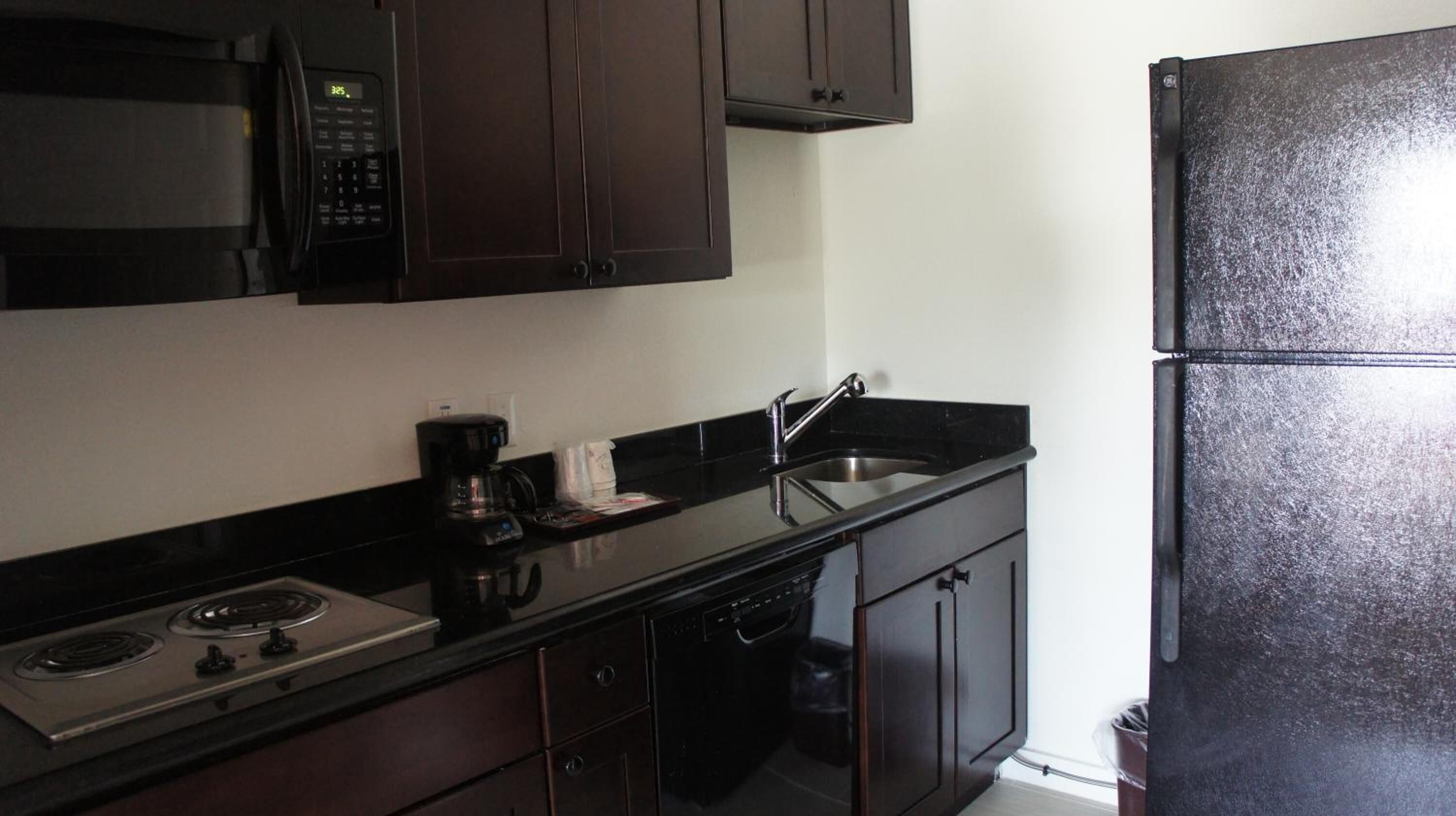 A compact kitchen with dark cabinetry, a microwave, a coffee maker, a sink, and a refrigerator.