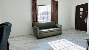 A room with a sofa, a door with a sign, and a window with curtains. - Lux Inn and Suites (Three Rivers)